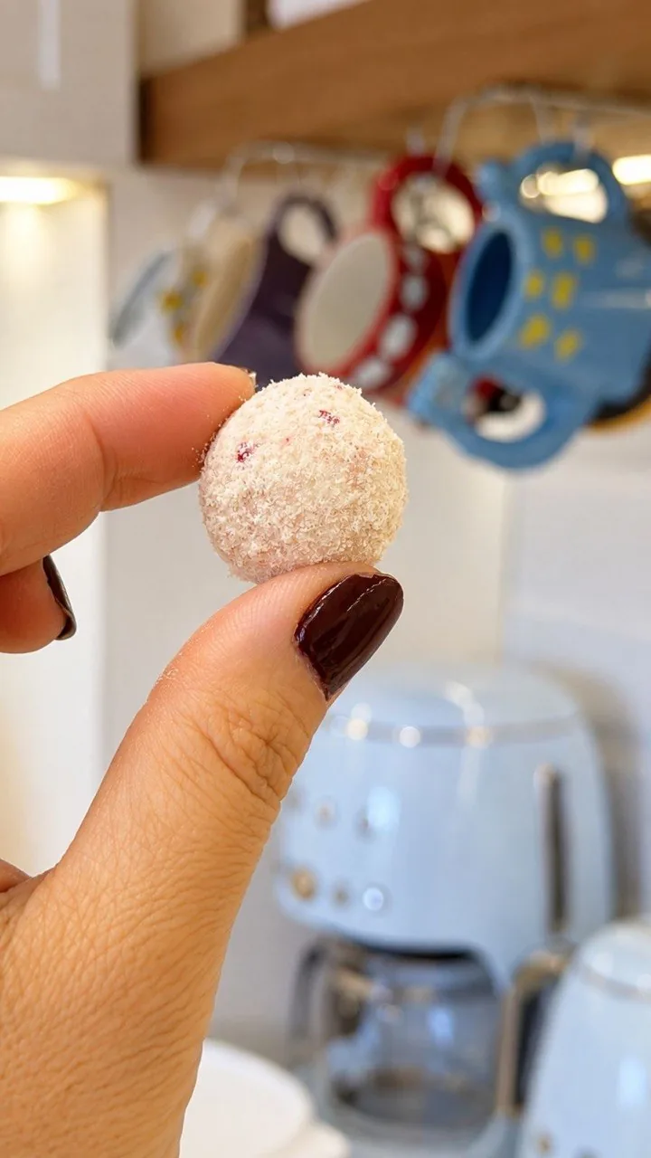 Close de uma bolinha do biscoito do amor cravejado entre os dedos